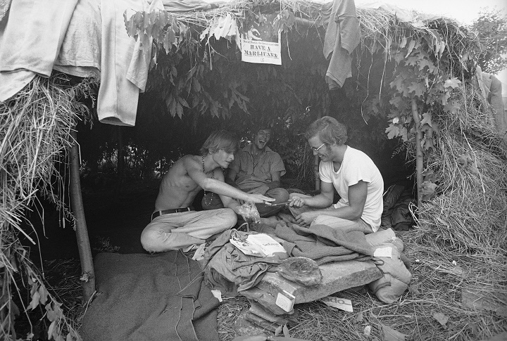 Music fans seek shelter is a grass hut at the Woodstock Music and Art Festival in Bethel, New York, Aug. 17, 1969. Sign above reads "Have a Marijuana." (AP Photo)